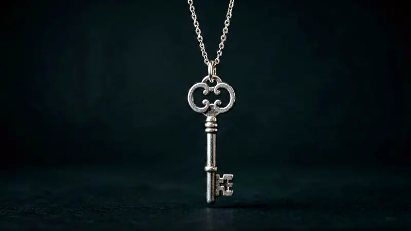 Silver key charm hanging from a delicate chain against a dark background